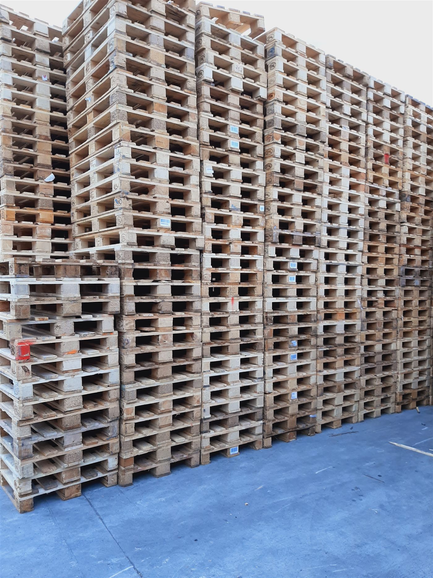Stacks of used wooden pallets on a blue warehouse floor